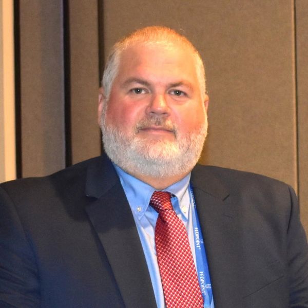 Man in a suit with a red tie and white beard.