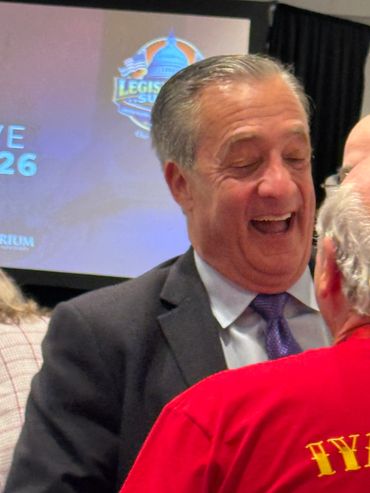 Two men joyfully interacting at an event with a presentation screen in the background.