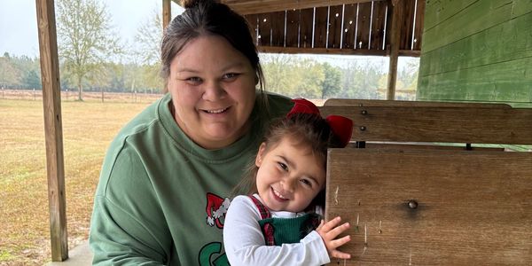 Smiling woman and child posing outdoors on a porch.