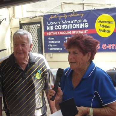 Two elderly people speaking with a microphone at an event.