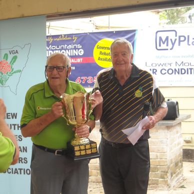 Two elderly men holding a large trophy and smiling, celebrating a win.