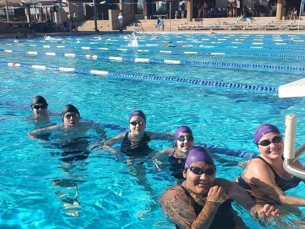 Six swimmers in purple caps posing in a pool lane.