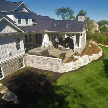An outdoor living space with hottub, covered patio & fire place, outdoor kitchen, and dining area. 