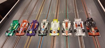 Eight colorful slot cars lined up on a racing track ready to race.