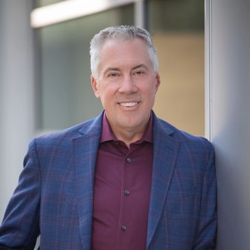 Middle-aged man in a blue checkered blazer and maroon shirt smiling.