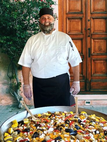 Chef standing behind a large pan of seafood paella.