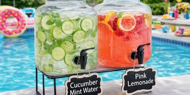 Two beverage dispensers with cucumber mint water and pink lemonade by a pool.