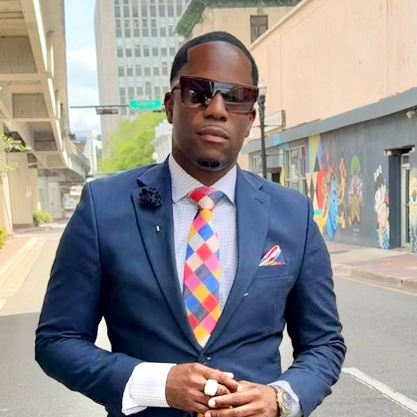 Confident man in a navy suit and colorful tie stands on a city street.
