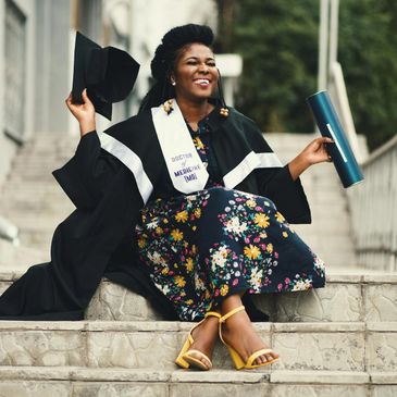 Joyful graduate woman in cap and gown holding diploma outdoors.