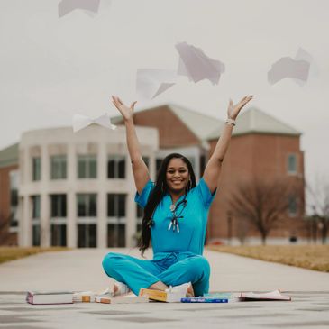 A joyful nurse in blue scrubs throws papers in the air outdoors.