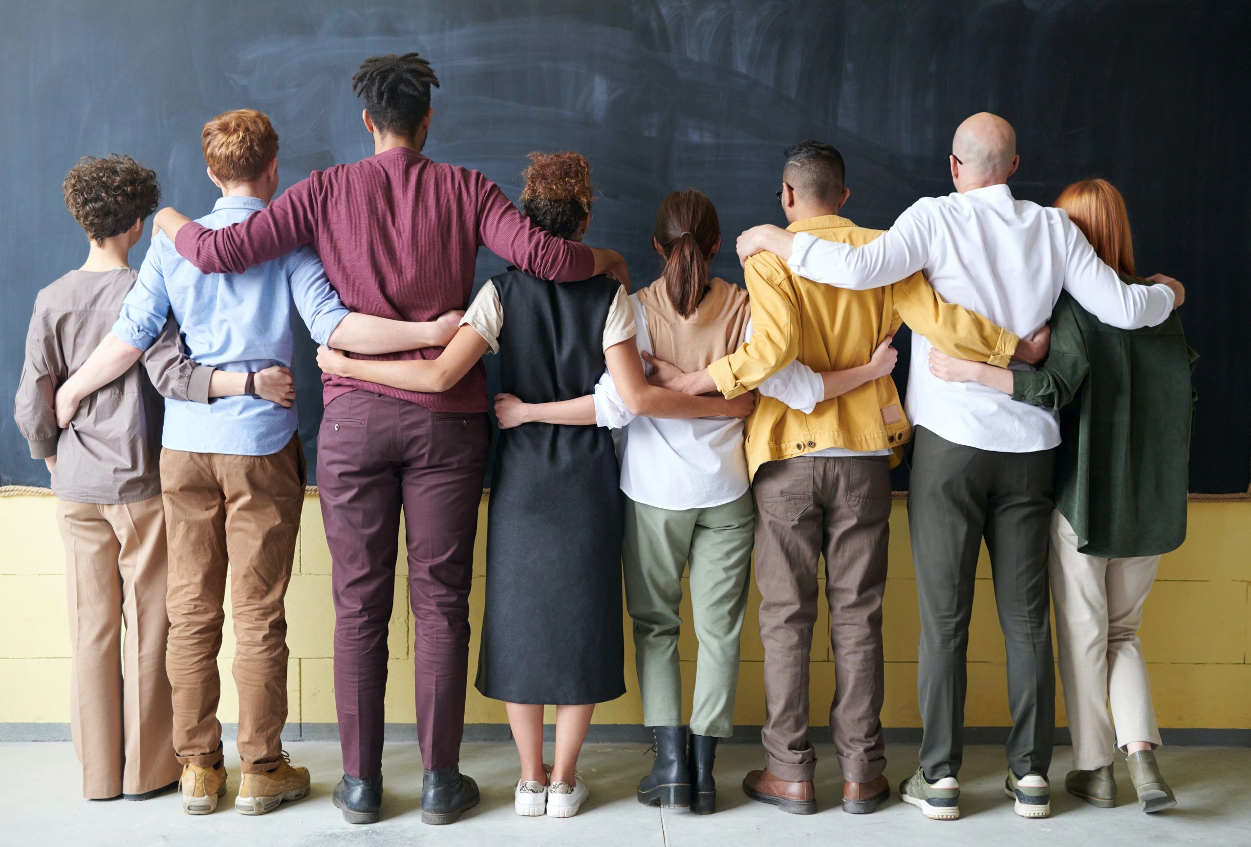 a line of eight people holding each other in front of a blackboard 