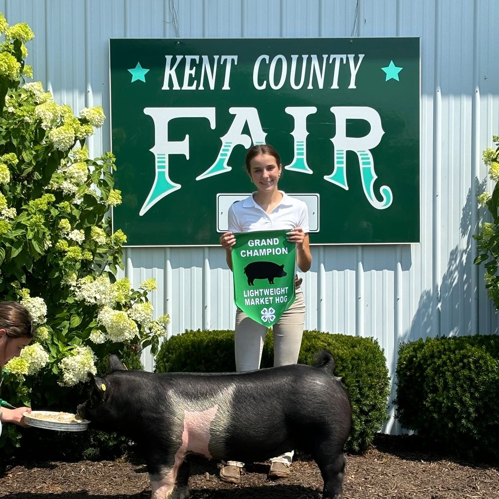 Young girl holds grand champion banner at Kent County Fair with her market hog.