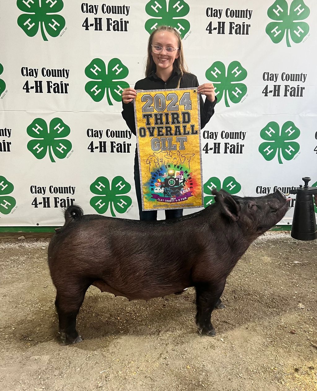 Young girl holds a banner for third overall gilt at Clay County 4-H Fair.
