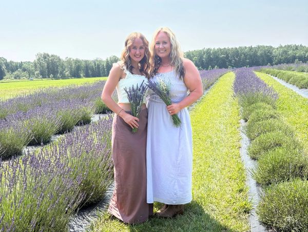 Two women holding lavender bouquets in a sunny lavender field.