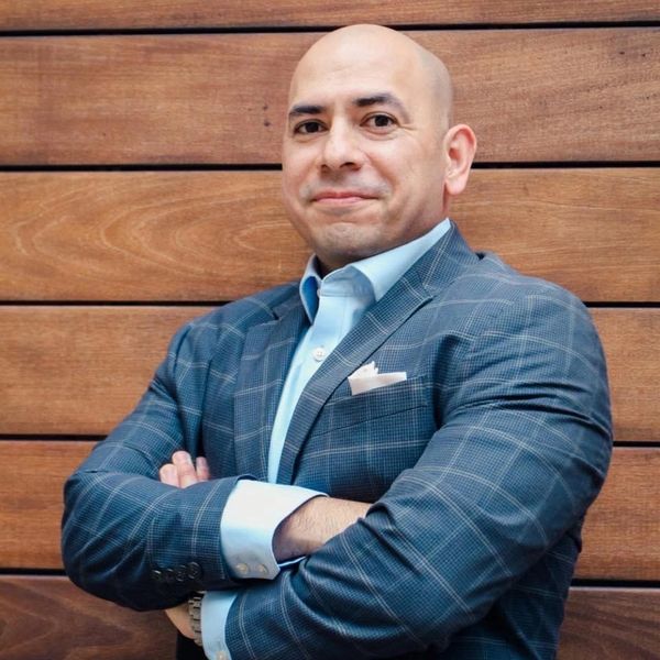 Confident man in checkered blazer poses with arms crossed.