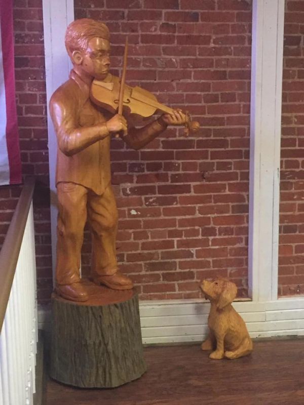 Wooden sculpture of a boy playing violin with a dog sitting nearby - Yesterday's in Boonville, IN