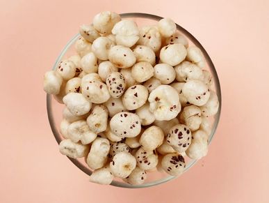 A bowl filled with puffed lotus seeds on a pink background.