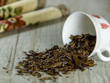 Loose tea leaves spilled from a white cup onto a wooden surface.
