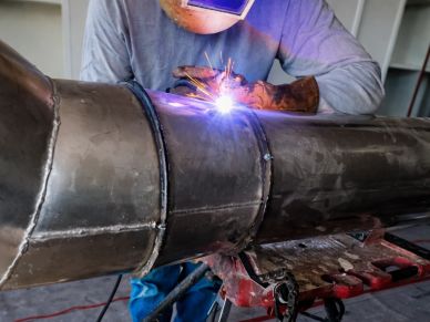 Welder working on a large metal pipe with sparks flying.