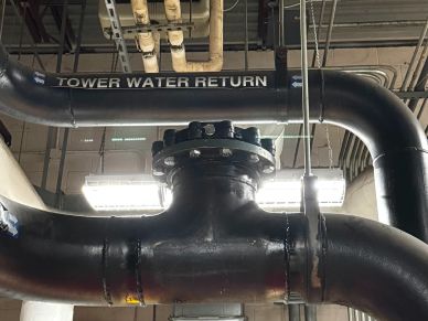 Large black pipes labeled "Tower Water Return" in an industrial setting.