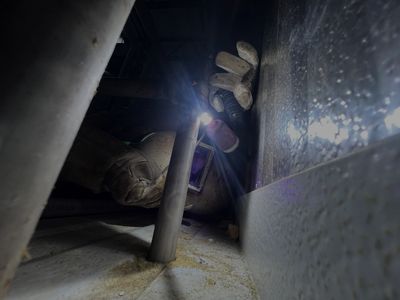 A person working in a confined space with a flashlight and gloves.