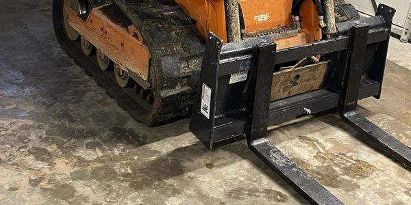 Close-up of a forklift attachment on heavy machinery with tracks.