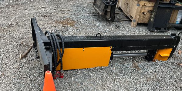 Industrial hydraulic equipment part resting on gravel with an orange safety cone nearby.