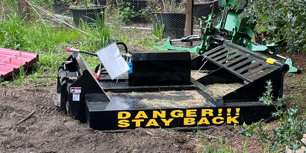 A black machine with a yellow warning sign saying 'DANGER!!! STAY BACK' in a garden.