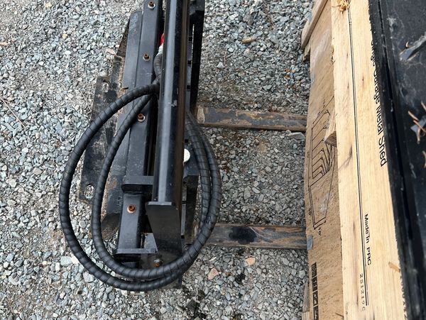Close-up of a forklift's hydraulic system and wooden pallet on gravel.