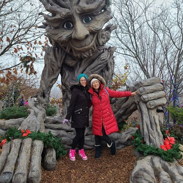 Two women posing in front of a large tree-like statue.
