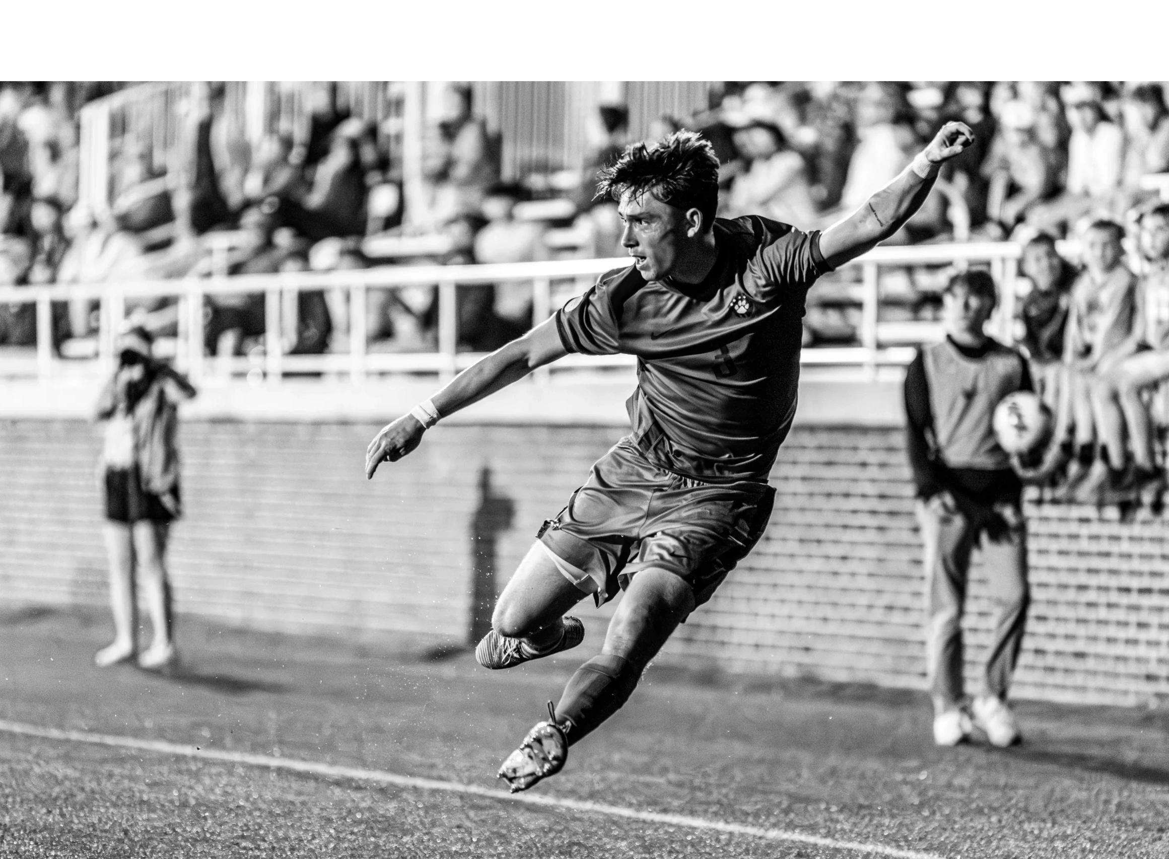 Soccer player in mid-air kicking the ball during a match with spectators in the background.