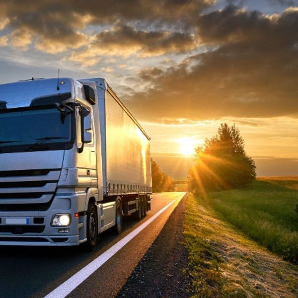 A large truck driving on a road at sunset with sun rays and clouds.