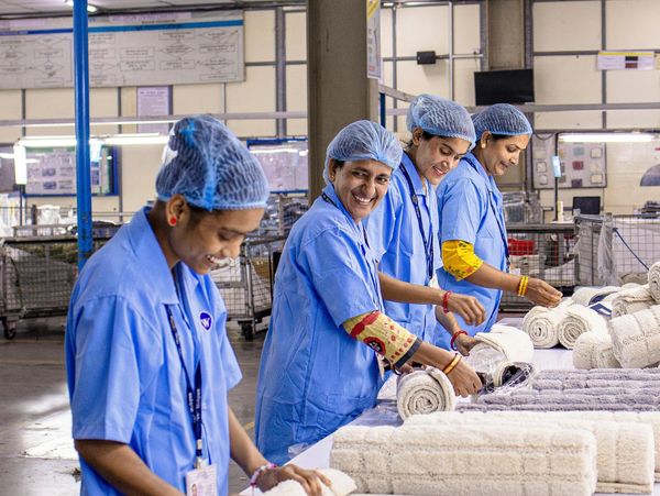 Women in blue uniforms rolling towels in a factory setting.