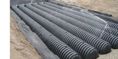 Installation of large black drainage pipes in a sandy trench.