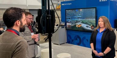 Woman being interviewed at a tech event with a gaming display.