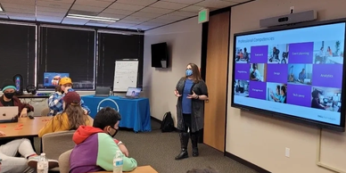 Instructor teaching a classroom with a presentation on a screen.
