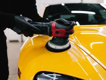 Person polishing a yellow car with an electric buffer.