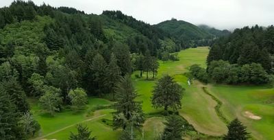 A lush green golf course surrounded by trees and hills.