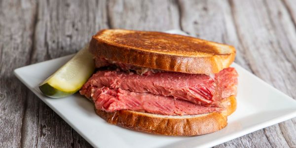 Close-up of a pastrami sandwich with a pickle on the side.