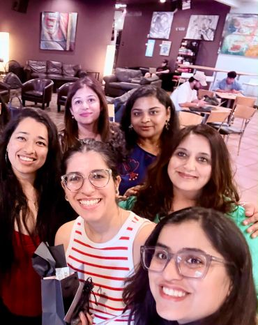 Group of six women smiling in a cozy cafe.