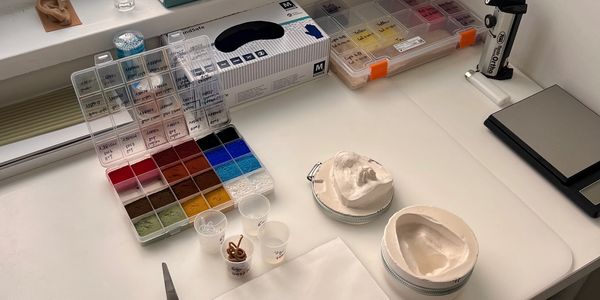 A clean workspace with dental molds, pigments, tools, and a plant by the window.