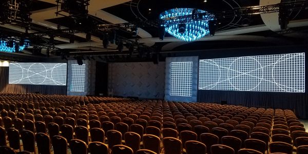 Empty conference hall with rows of chairs and large screens.