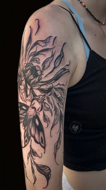 Black ink tattoo of a flower and butterfly on upper arm.