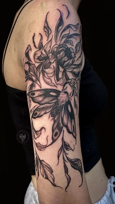 Black ink tattoo of a moth and flowers on upper arm.