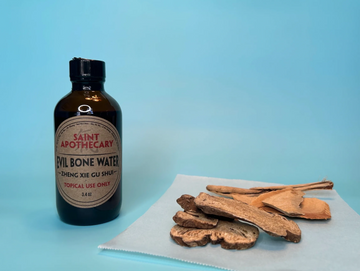 bottle of Evil Bone Water next to some raw herb ingredients 