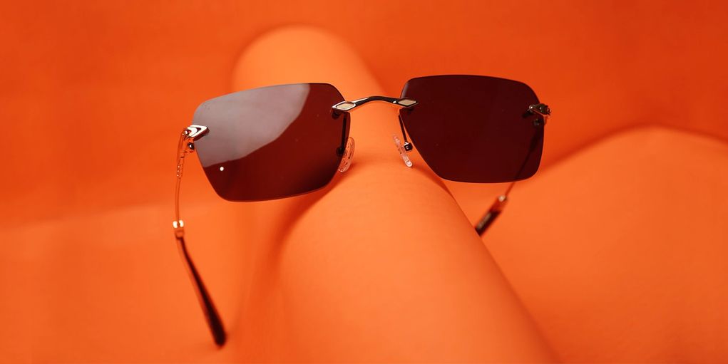 Stylish rimless sunglasses with dark lenses on an orange surface.