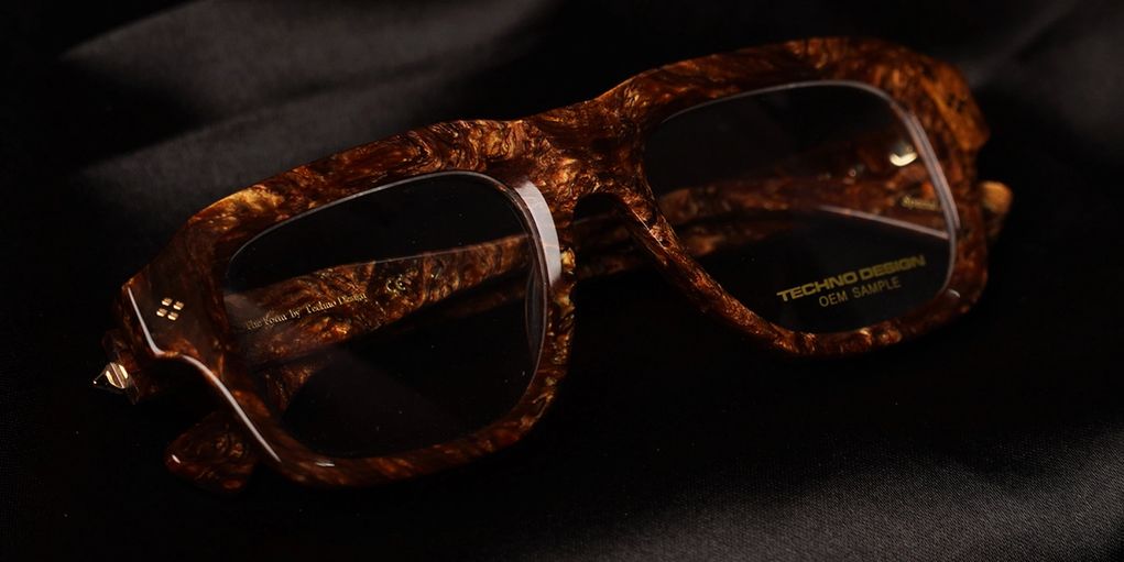 Close-up of brown marbled eyeglasses with Techno Design branding on a black surface.