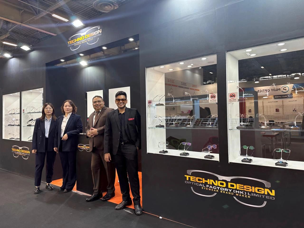 Four professionals stand in front of a Techno Design eyewear booth at a trade show.