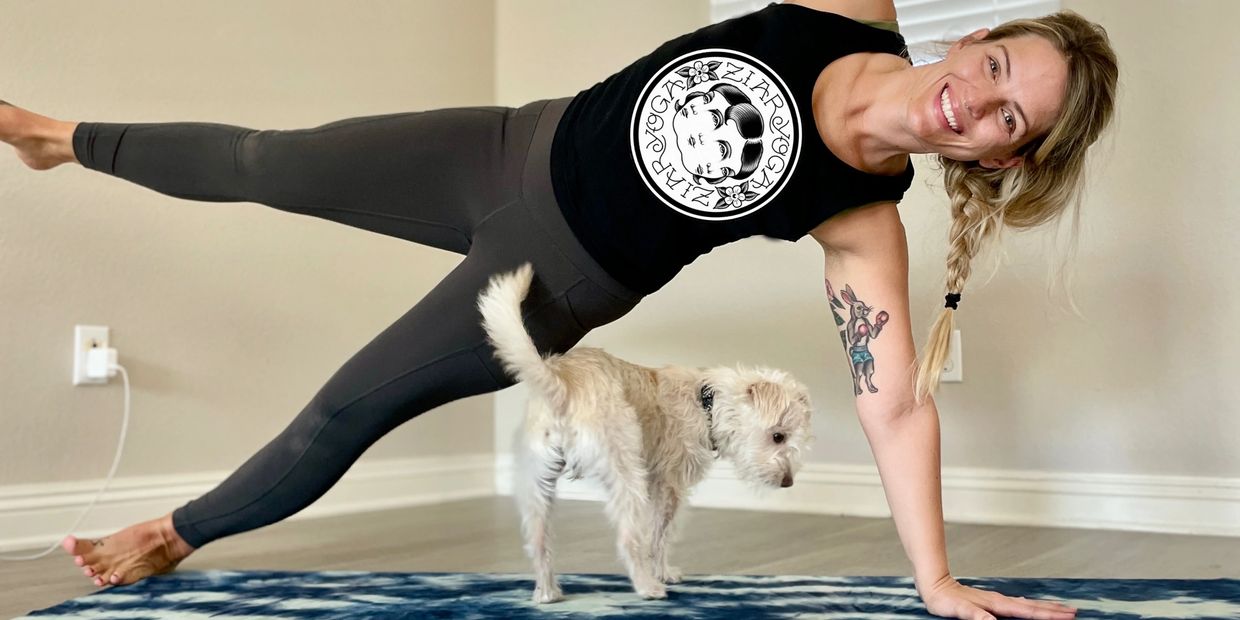 Woman smiling in side plank with her dog standing under her