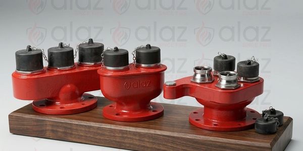 Red industrial valves with black caps mounted on a wooden base.